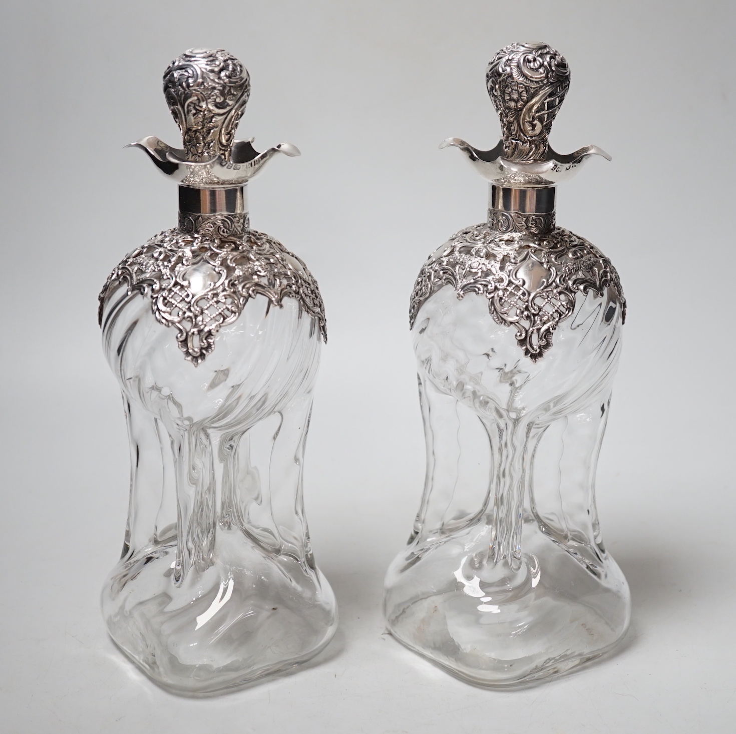 A pair of late Victorian repousse silver mounted hour glass decanters and stoppers, Henry Matthews, Birmingham, 1899, height 25mm.